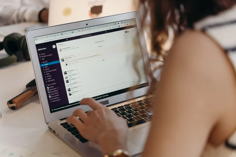A woman working on a laptop with a team chat on screen — illustration for an article about HRM systems
